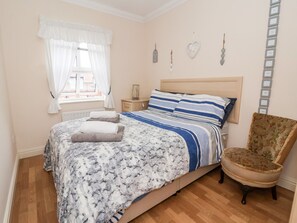 Un dormitorio con cama, una silla, una mesita de noche y una ventana con cortinas.