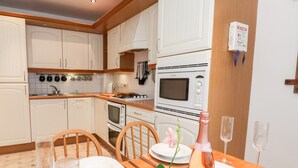 Una cocina moderna con armarios blancos, estufa a gas, horno y microondas. Hay una mesa de comedor con platos, vasos y cubiertos.