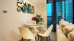Un salon moderne avec une table à manger en verre, deux chaises, un canapé et un mur décoratif agrémenté d’un miroir.