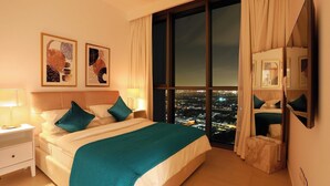 Une chambre d’hôtel avec un grand lit, deux tables de chevet, une commode, une grande fenêtre donnant sur la ville et un miroir.