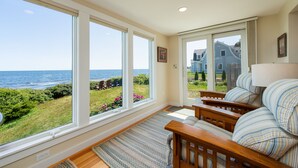 A room with large windows offering a view of the sea and a grassy area with chairs and a table. - Sea Spray - Beautiful 2BR, 1BA cottage with expansive views of Casco Bay (Bailey Island)