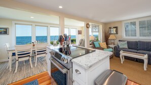 A kitchen with a large island, dining area with chairs, and a view of the ocean. - Sea Spray - Beautiful 2BR, 1BA cottage with expansive views of Casco Bay (Bailey Island)