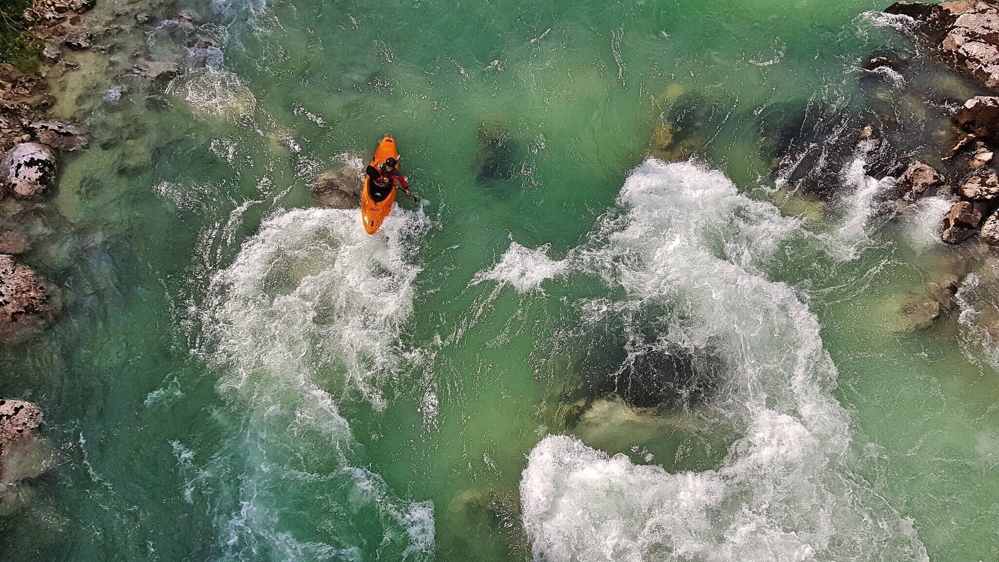 Ein Kajakfahrer auf einem klaren Fluss mit steinernen Ufern.