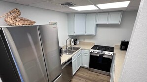 A compact kitchen with a stainless steel refrigerator, a gas stove, and light-colored cabinets. - Relax Inn - Seamist 156 (Port Aransas)