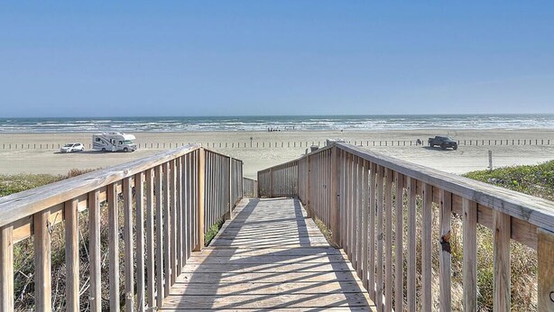 A wooden boardwalk leading to a beach with vehicles parked on the side. - Relax Inn - Seamist 156 (Port Aransas)