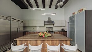 Una cocina moderna con una isla central, sillas de mimbre blancas, electrodomésticos de acero inoxidable y techo de madera.