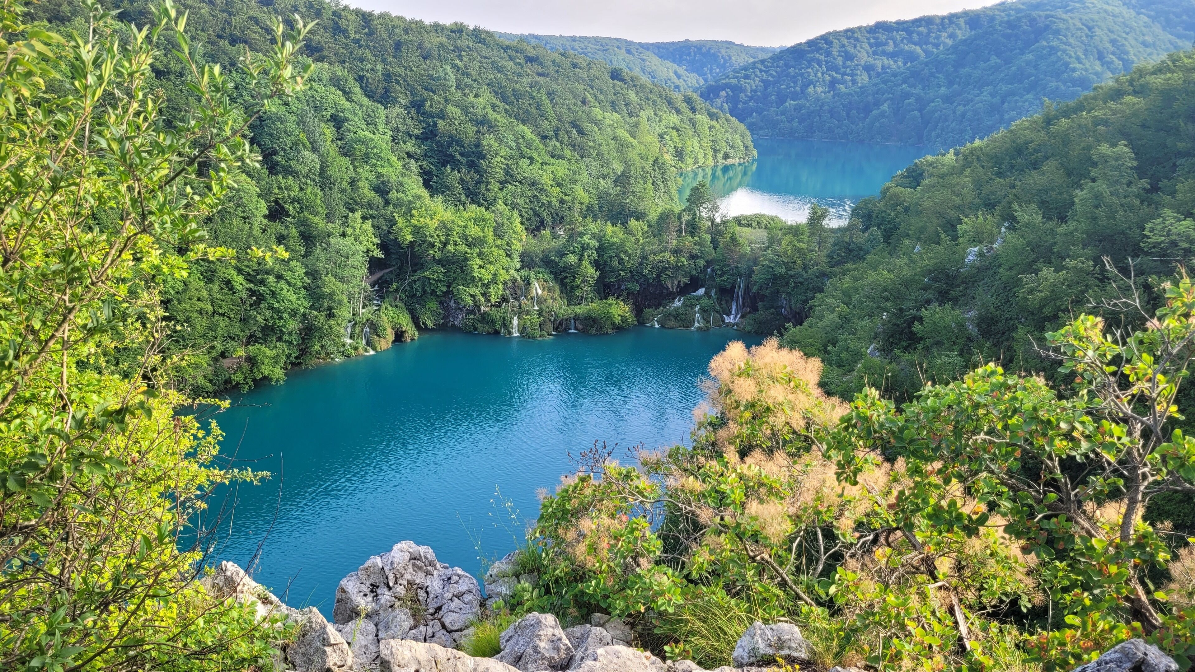 Paisaje montañoso con un lago rodeado de un bosque denso y afloramientos rocosos.