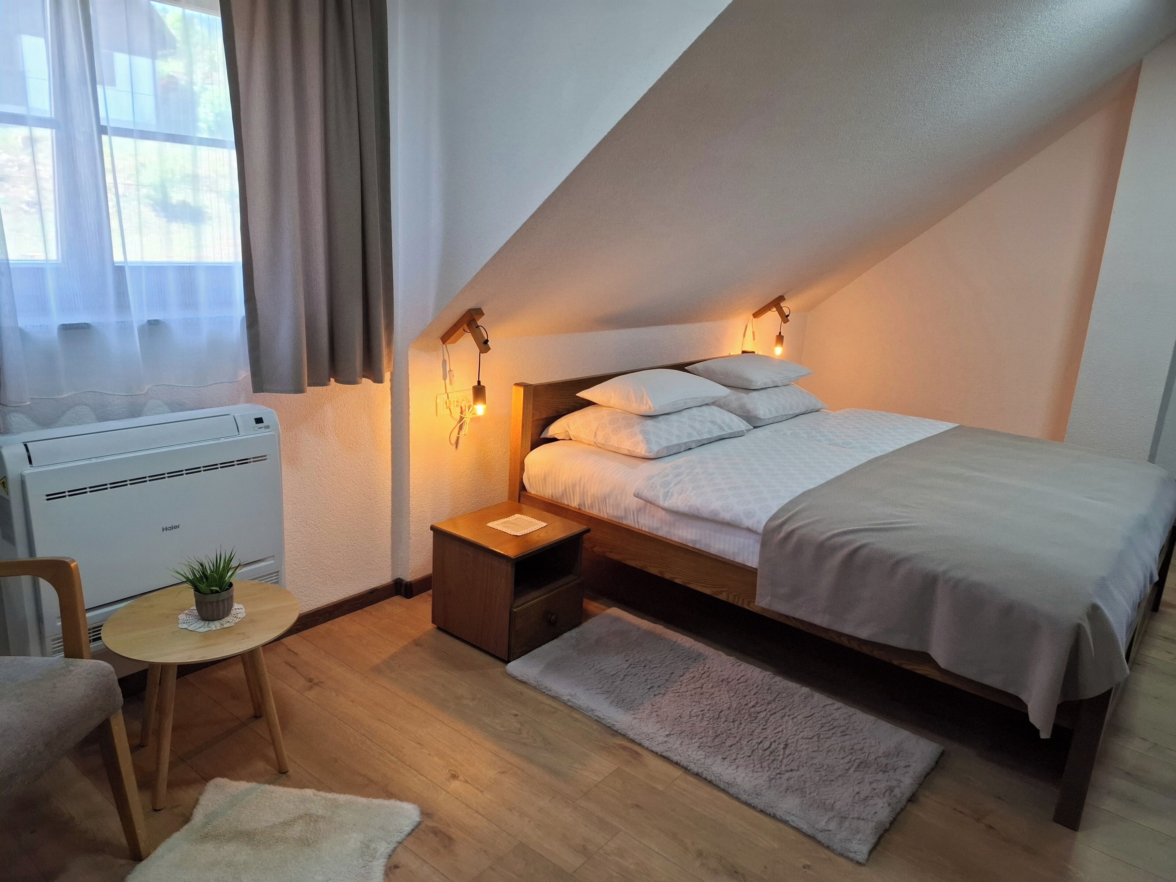 A cozy room with a bed, bedside table, lamp, chair, and a small table with a plant.