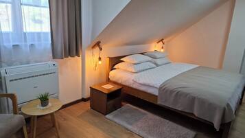 Ein gemütliches Zimmer mit Bett, Nachttisch, Lampe, Sessel und einem kleinen Tisch mit einer Pflanze.