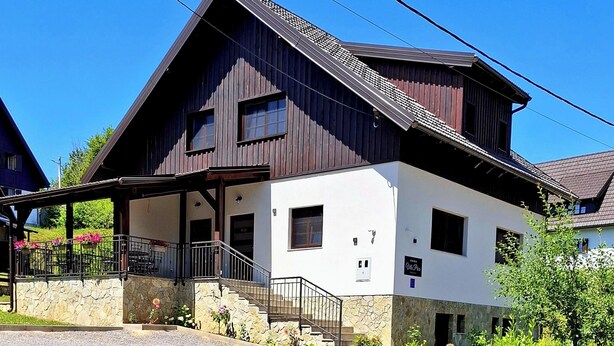 Edificio de dos pisos con base de piedra y estructura superior de madera. Un letrero indica que es una "Villa Prica" y ofrece servicios como camas, estacionamiento y restaurante.