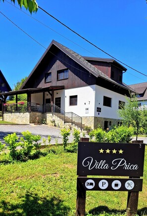 Edificio de dos pisos con base de piedra y estructura superior de madera. Un letrero indica que es una "Villa Prica" y ofrece servicios como camas, estacionamiento y restaurante.