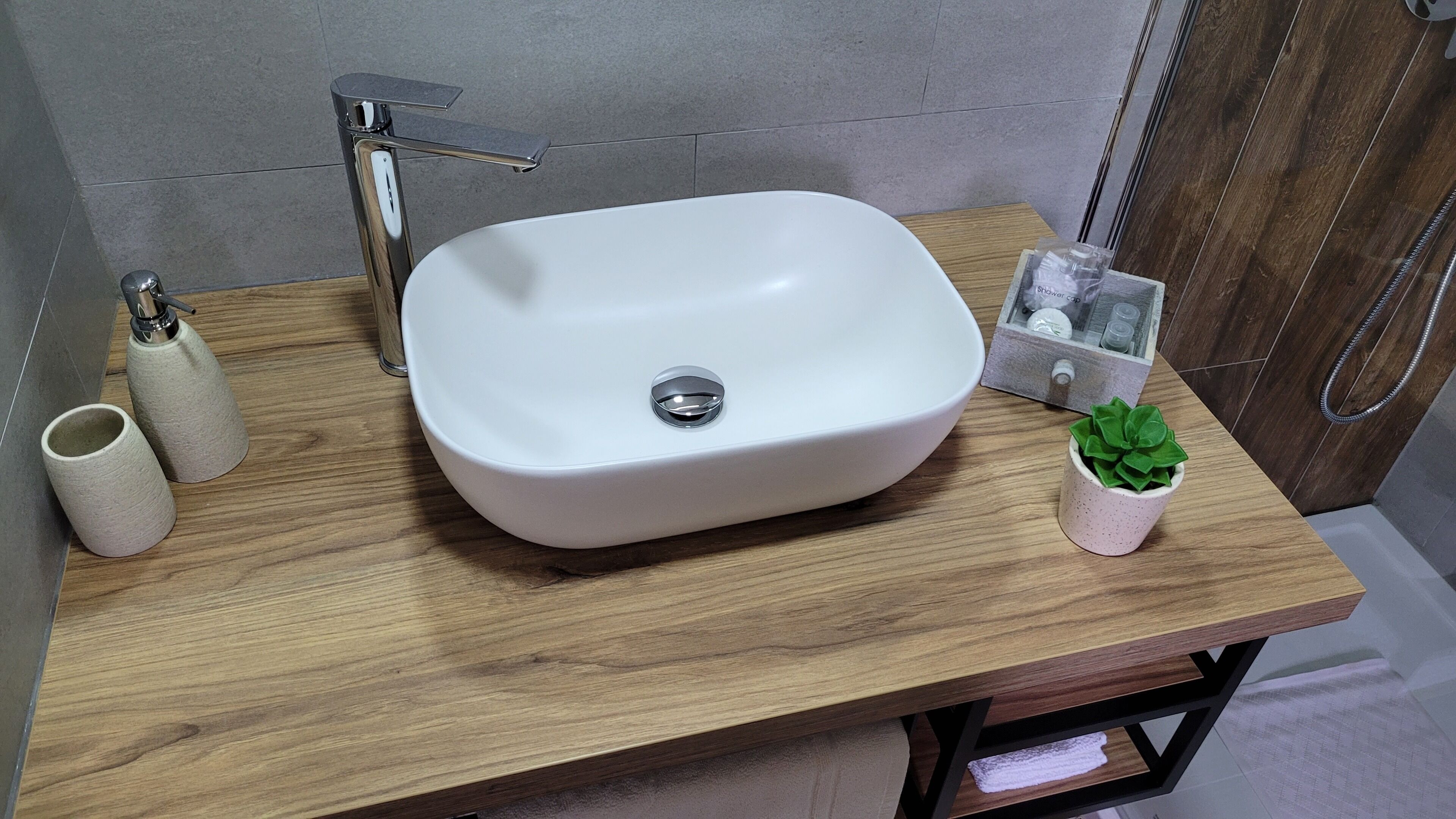 A bathroom with a white sink, a wooden vanity, a small potted plant, and a shower caddy.