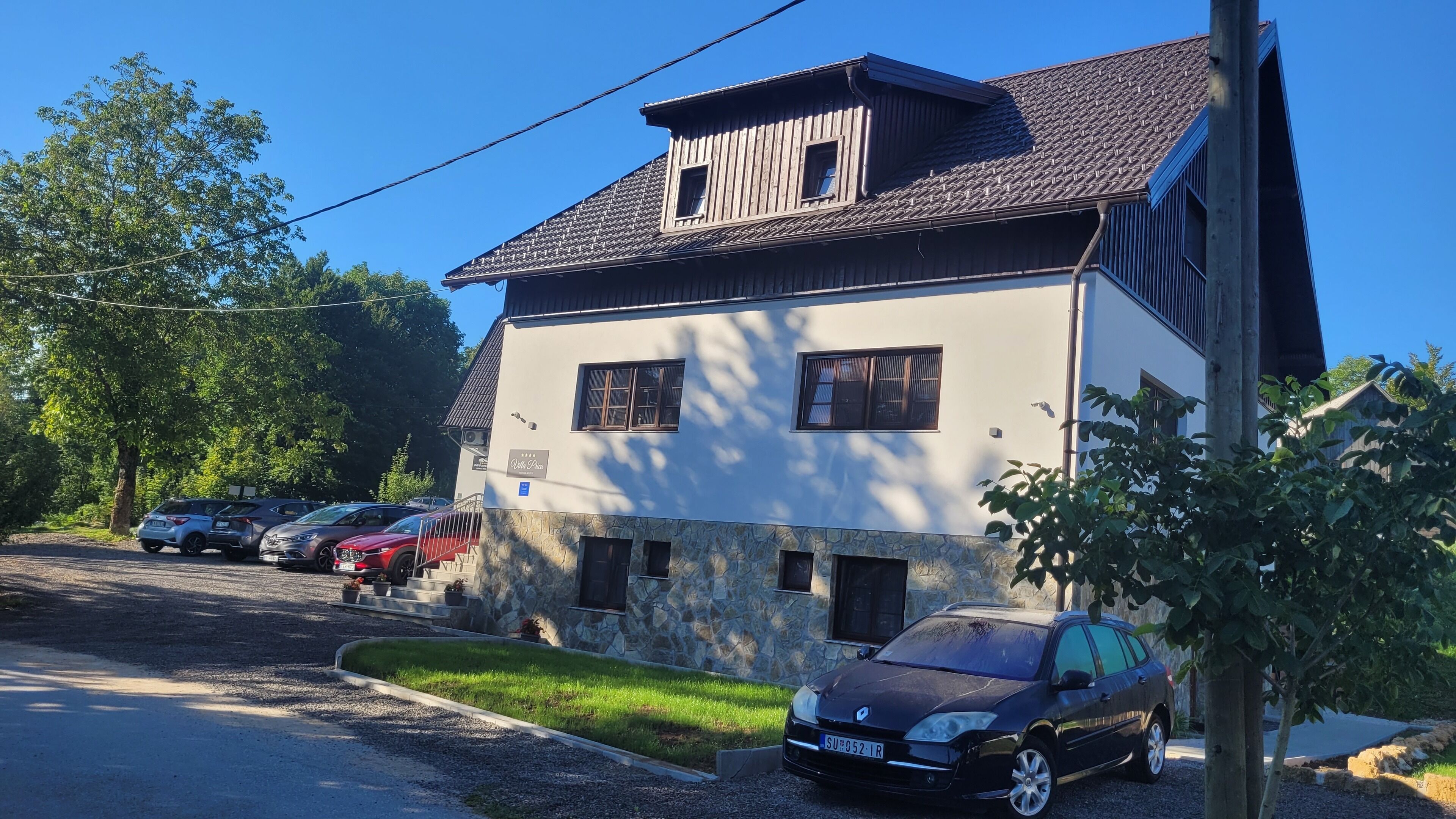 A two-story building with a stone facade and a tiled roof. There are several parked cars in front.