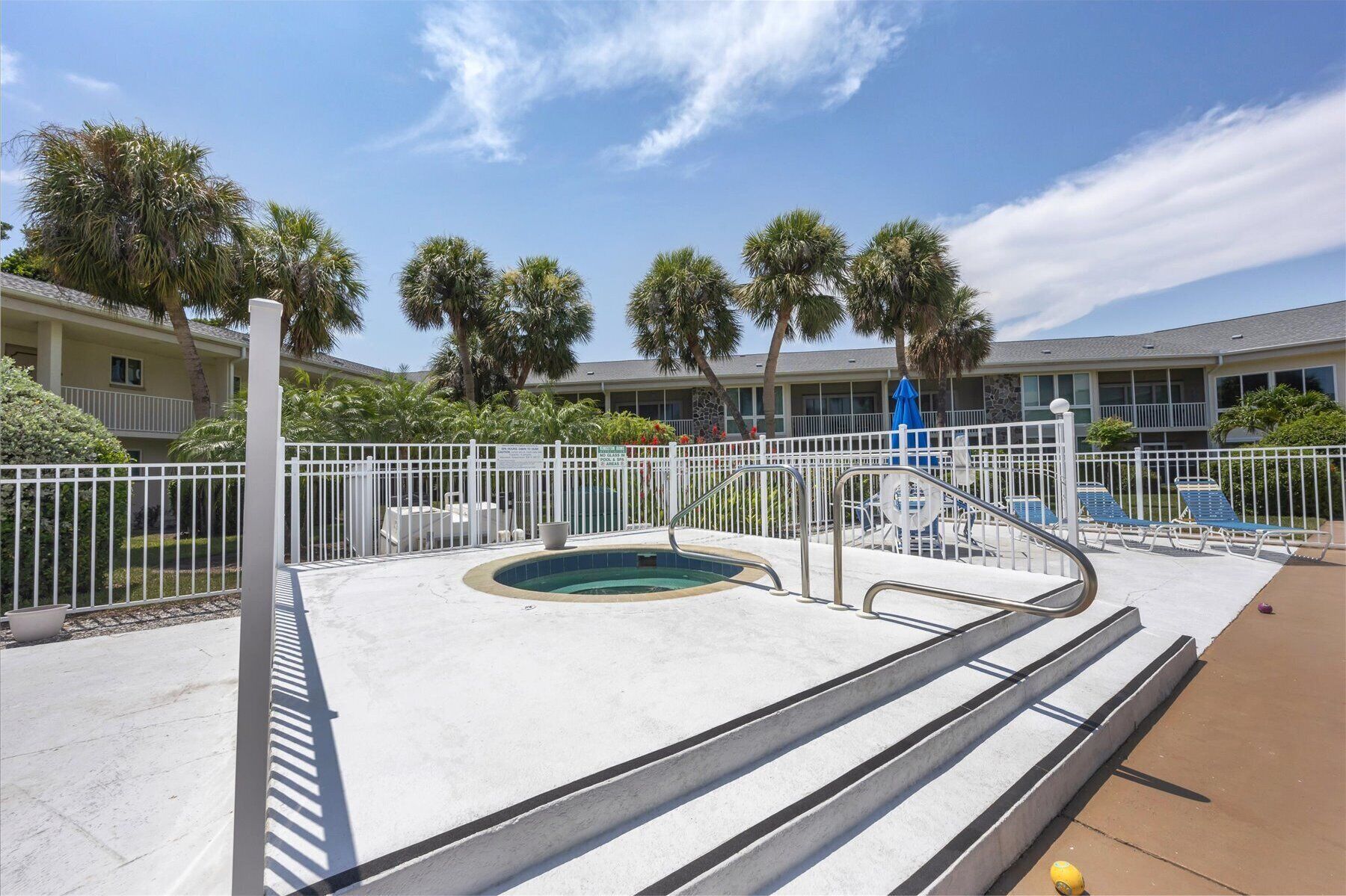 Un área de piscina con jacuzzi, escalones que bajan a la piscina y sillas de descanso.