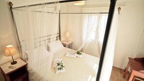 Ein Bett mit Baldachin, ein Nachttisch mit Lampe und ein kleiner Tisch mit Blume.