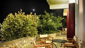 Eine Terrasse im Freien mit Steinboden, Holzstühlen, einem runden Tisch und einer Steinwand.