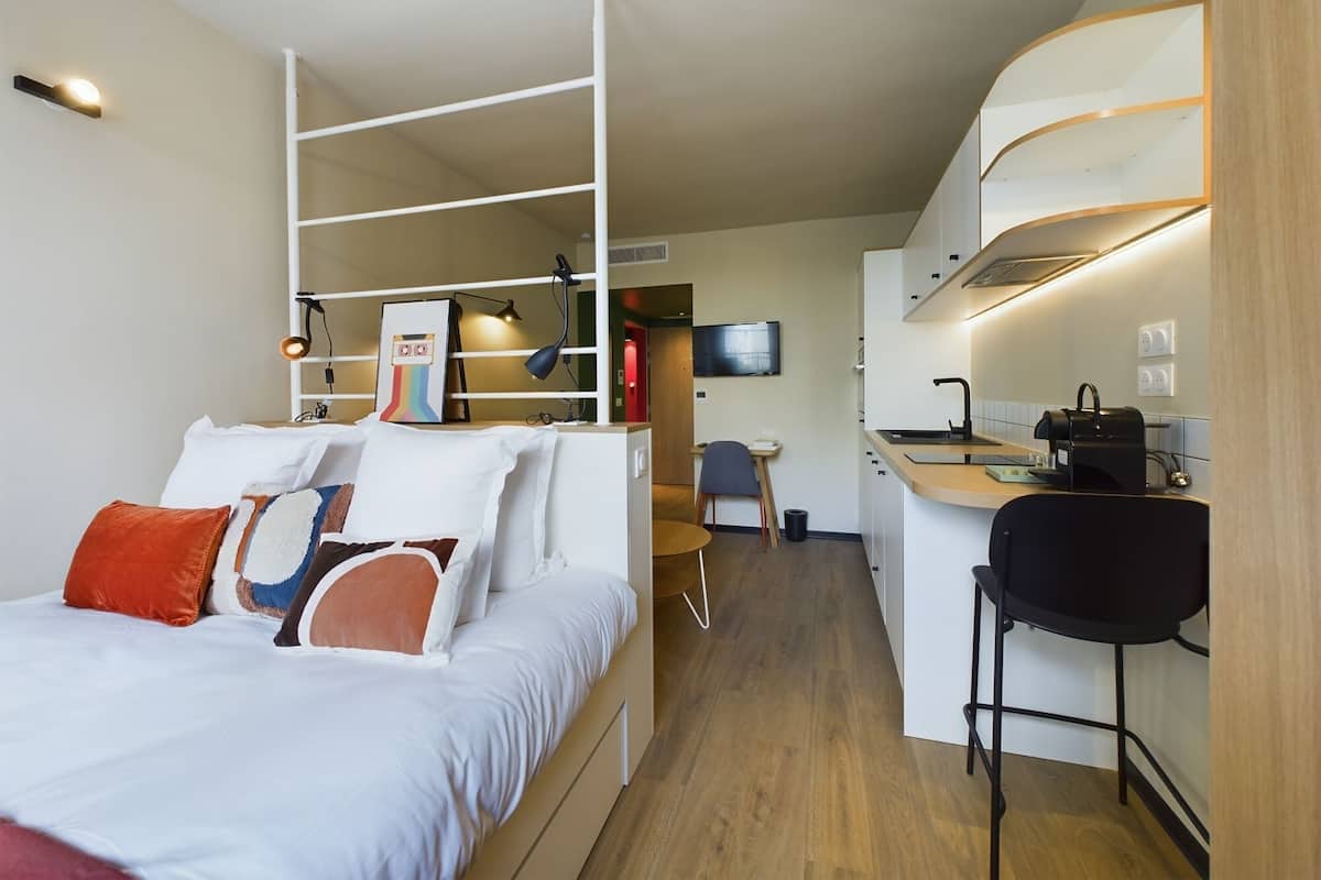 A compact hotel room with a bed, a desk, and a kitchenette.