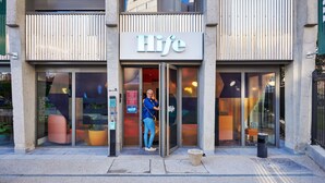 A building with a 'Hlife' sign, a glass door entrance, and a small outdoor seating area with planters. - Hife Paris Gentilly (Gentilly)