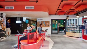 A modern workspace with red seating, people working on laptops, and a wall with various items and a sign that reads "WALLHUGER". - Hife Paris Gentilly (Gentilly)