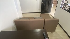 A modern living room with a sofa set, a TV mounted on the wall, and a wooden door leading to another room. - Barkada Room- New Apartment in Palompon (Palompon)