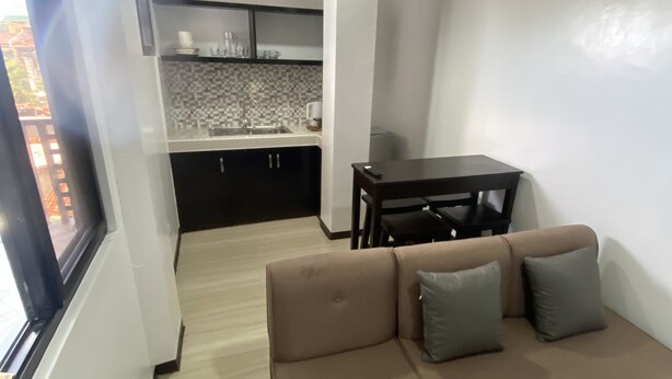 A modern living room with a brown sectional sofa, a small table, and a kitchen in the background. - Barkada Room- New Apartment in Palompon (Palompon)