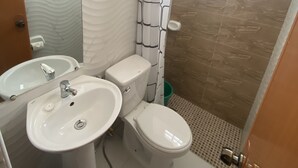 A bathroom with a sink, toilet, and shower area. There is a towel rack with towels above the toilet. - Barkada Room- New Apartment in Palompon (Palompon)