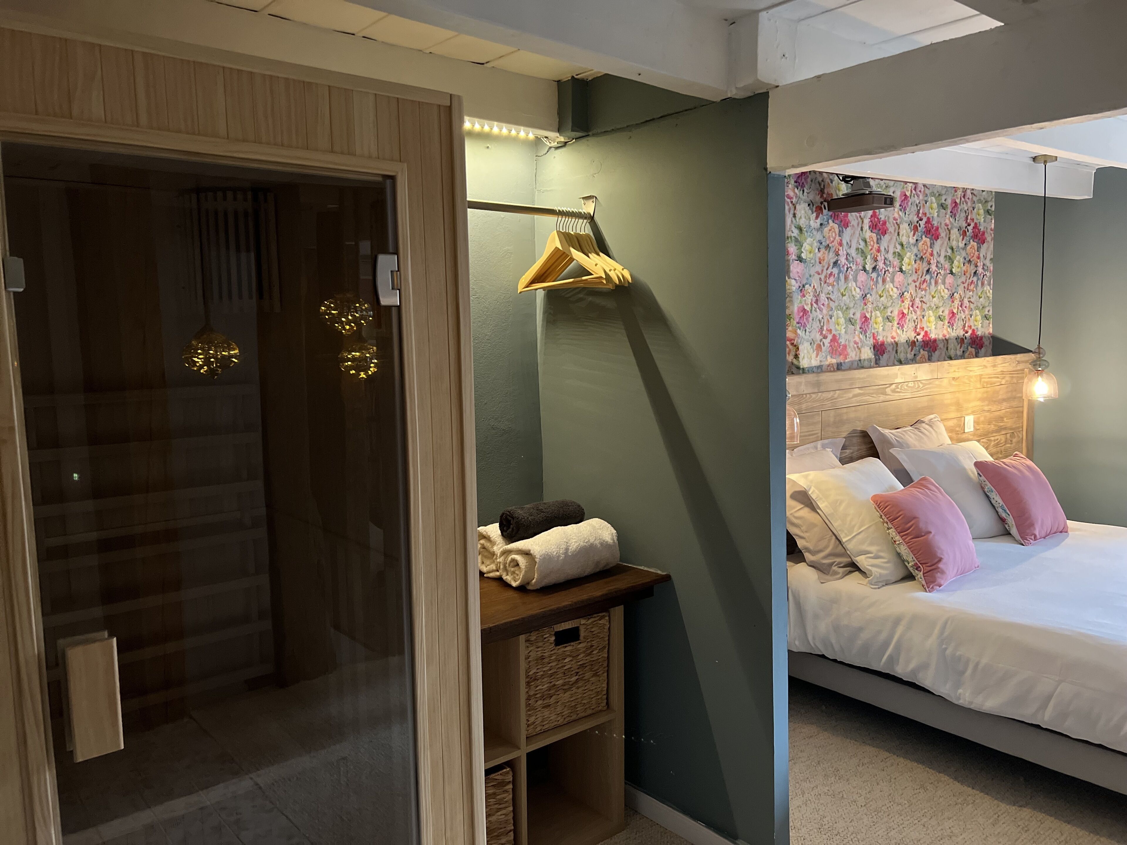 Un dormitorio con cama, almohadas, cabecera de madera, lámpara colgante y un adorno floral en la pared.