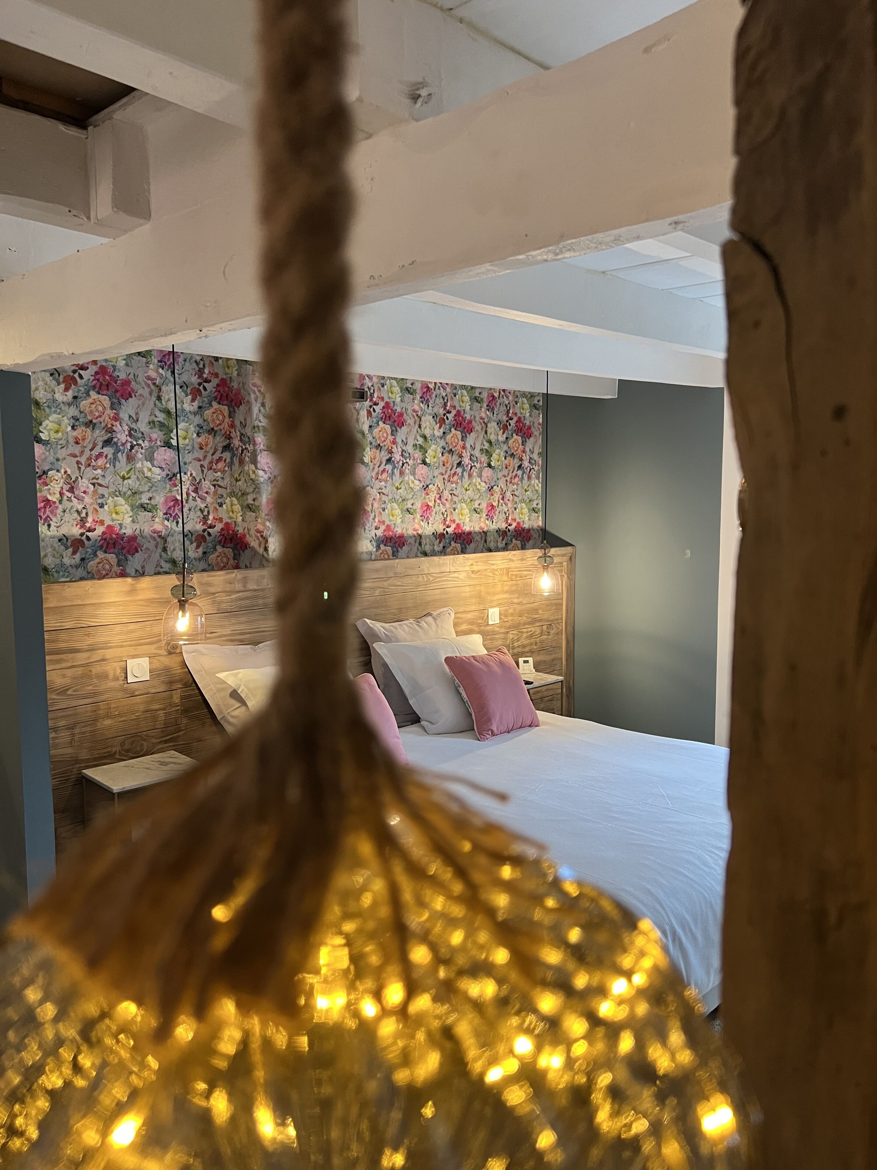 A bedroom with a wooden headboard, a floral wallpaper, and a bed with white and pink bedding.