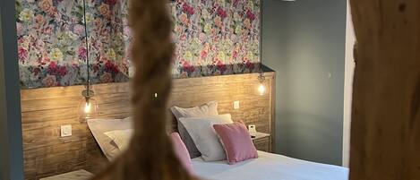 A bedroom with a wooden headboard, a floral wallpaper, and a bed with white and pink bedding.