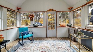 Ein Wintergarten mit großen Fenstern, einem blauen Sessel, einem Teppich und einem kleinen Tisch.