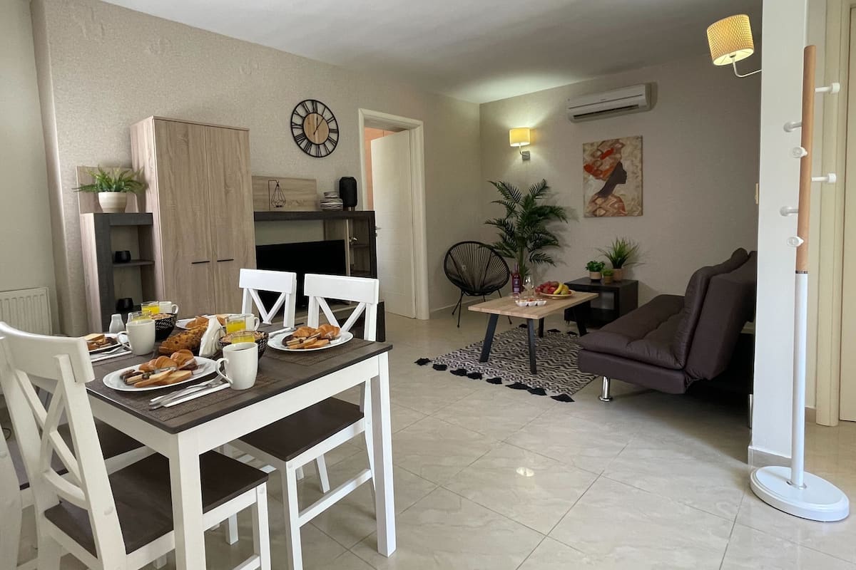 Un coin repas avec une table dressée pour deux personnes, des chaises et une horloge au mur.
