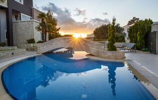 Una piscina con un puente de piedra, rodeada de edificios modernos y vegetación.