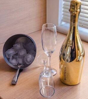 A bottle of Bottega Gold champagne, a bowl of ice cubes, and two wine glasses on a wooden surface. - Artdeco Luxury Suites (Chania)