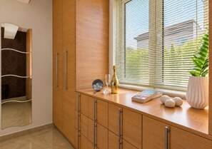 A modern kitchen with wooden cabinets, a countertop, a window with blinds, a potted plant, and a bottle of champagne. - Artdeco Luxury Suites (Chania)