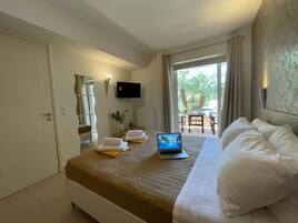Una habitación de hotel con cama, computadora portátil, televisor, silla y vistas al exterior.