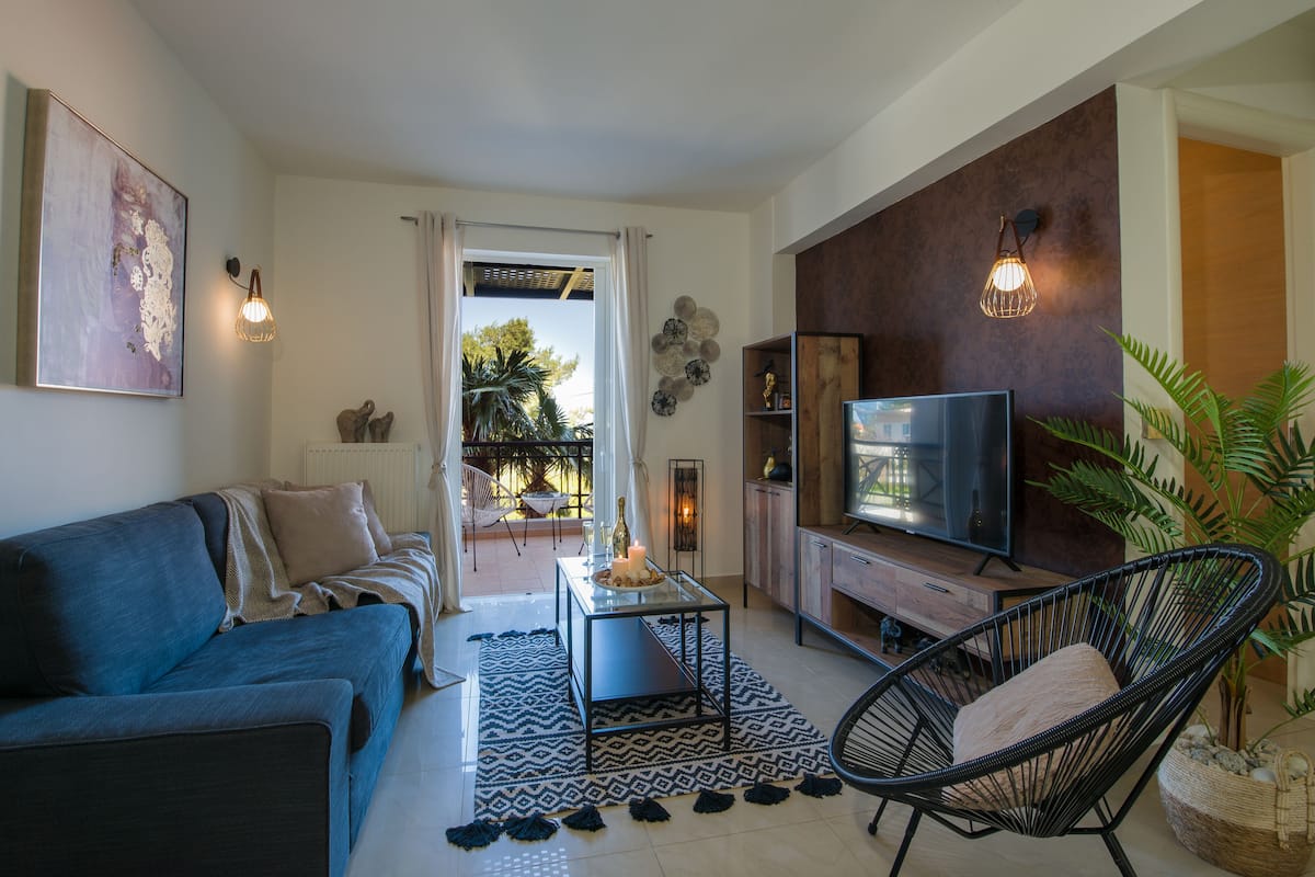 Un salon moderne comprenant un canapé, un téléviseur, un fauteuil et un coin repas avec une table et des bougies.