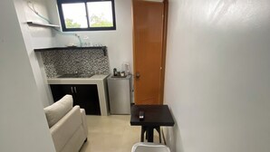 Un espace de vie compact comprenant un coin cuisine, un canapé, une table à manger avec une chaise, et une porte donnant sur une autre pièce.
