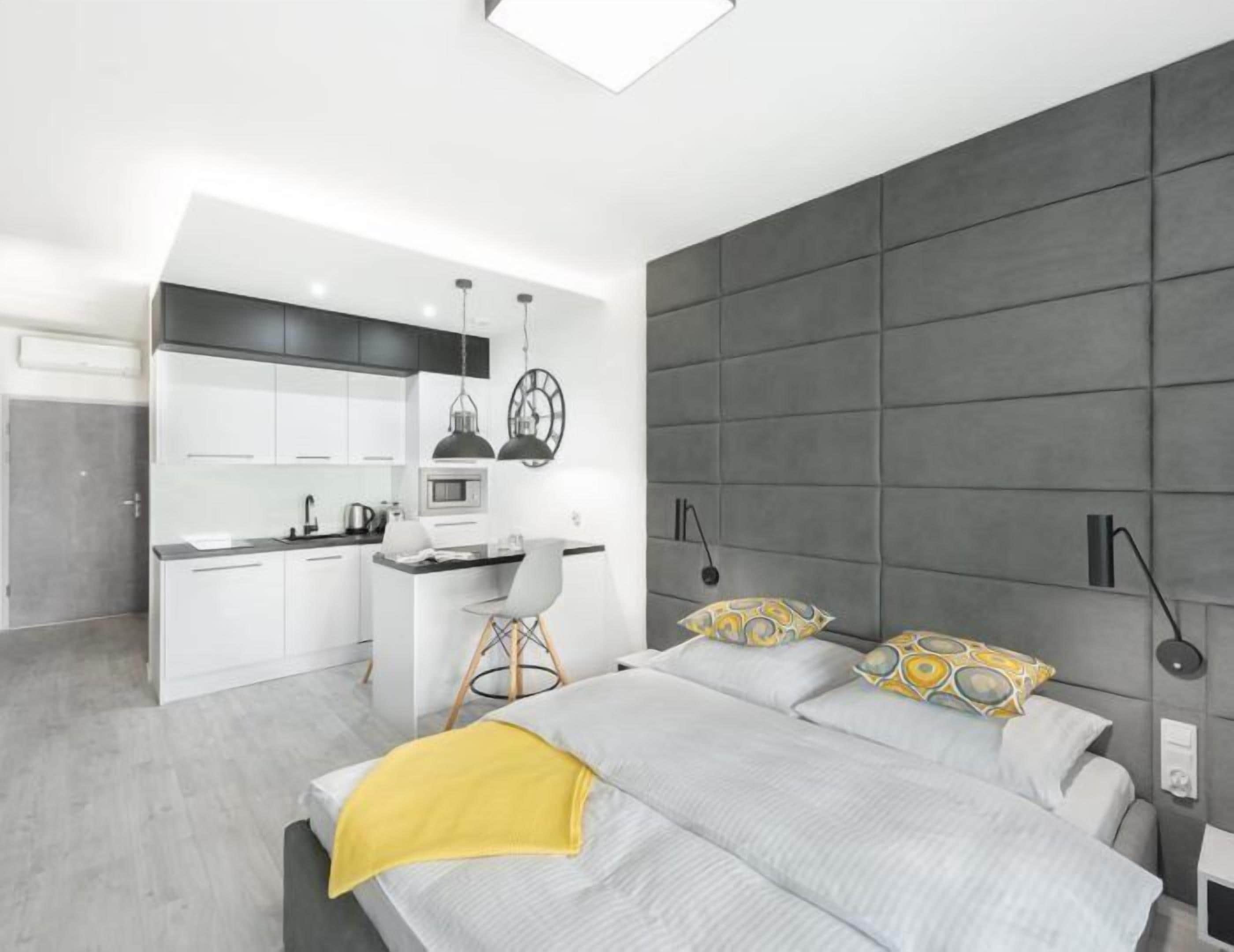 A modern bedroom with a large bed, a desk, and a kitchenette.
