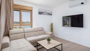Moderni olohuone, jossa on kulmasohva, sohvapöytä, televisio ja suuri ikkuna, josta on kaunis näkymä.