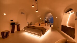 A modern bedroom with a large bed, a small table, and a unique arched ceiling design. - Twenty One Suites (Santorini)