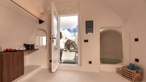 A modern bathroom with a bathtub, a sink, and a doorway leading to a balcony with a view of the sky and clouds. - Twenty One Suites (Santorini)