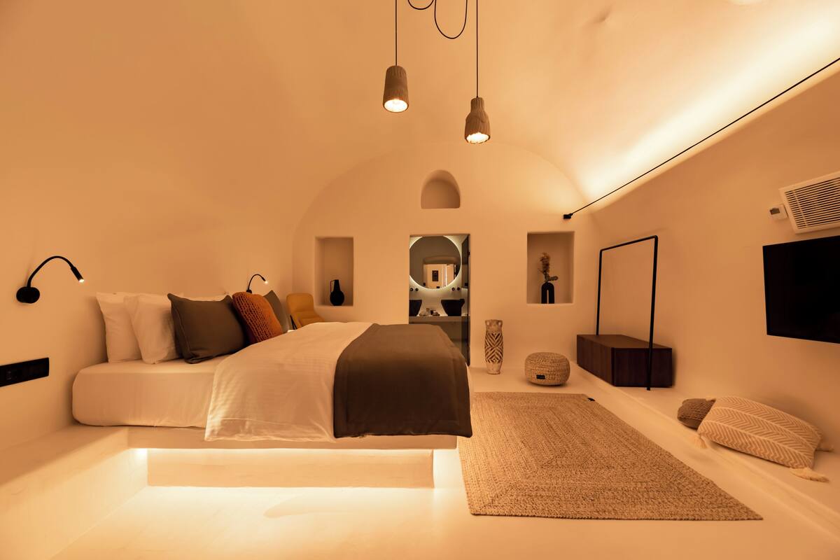 A modern bedroom with a large bed, bedside tables, a mirror, and a wall-mounted TV.