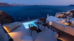 A terrace with a pool, dining area, and ocean view. - Twenty One Suites (Santorini)