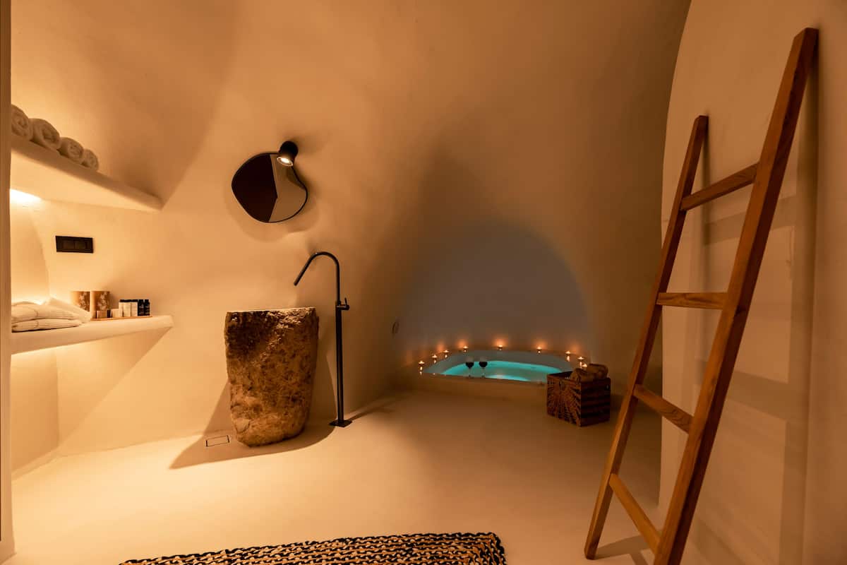 A modern bathroom with a freestanding bathtub, a wooden ladder, and a large stone basin.