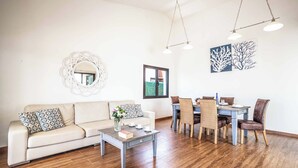 A living room with a sofa, coffee table, dining table with chairs, a mirror, and artwork on the wall.