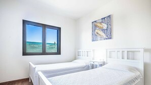 A bedroom with two single beds, a window with a view of the sea, and a wall-mounted artwork.