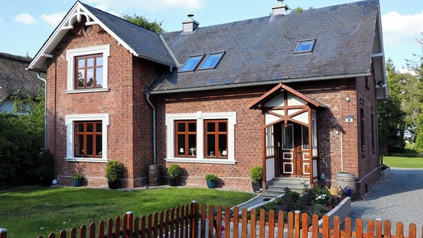 A two-story brick house with a gabled roof, dormer windows, and a wooden front door.