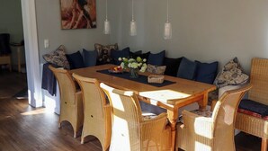 A dining area with a long wooden table, wicker chairs, and blue cushions.
