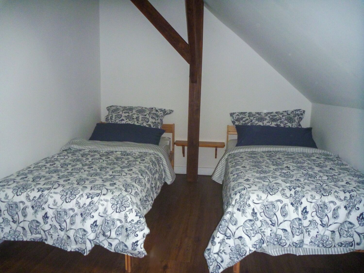 A small, single-room bedroom with two twin beds, each with patterned bedding and pillows.