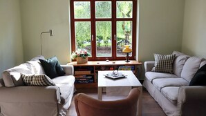 A living room with two sofas, a coffee table, and a window with a view of greenery.